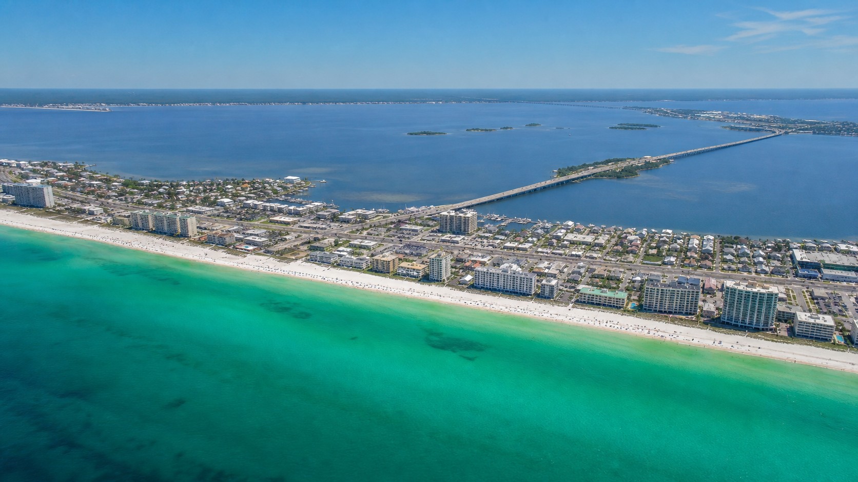 Aerial view of the Destin Florida coastline showing the narrow barrier island strip with Gulf on one side and Choctawhatchee Bay on the other, US-98 highway running through