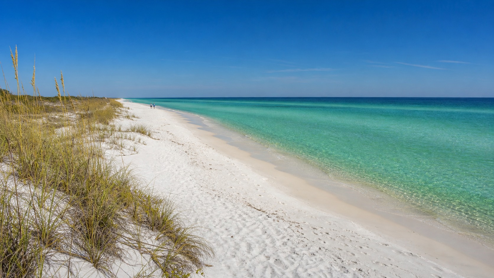 Pristine white sugar-sand Florida Panhandle beach with crystal clear emerald green water, undeveloped coastline, and blue sky