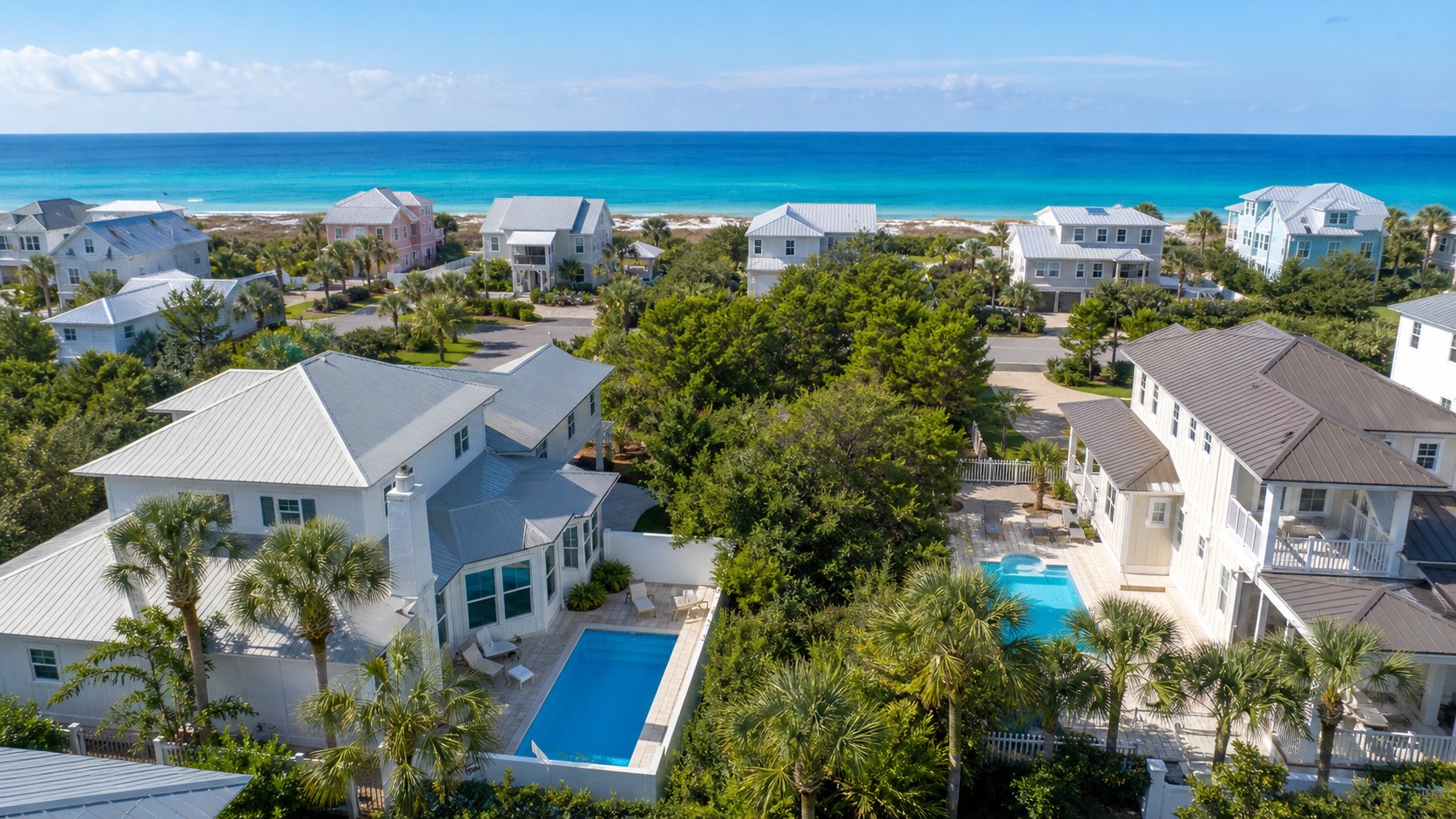Aerial view of vacation rental homes with bright blue private pools in a Miramar Beach Florida residential neighborhood surrounded by palm trees with the Gulf of Mexico visible in the background
