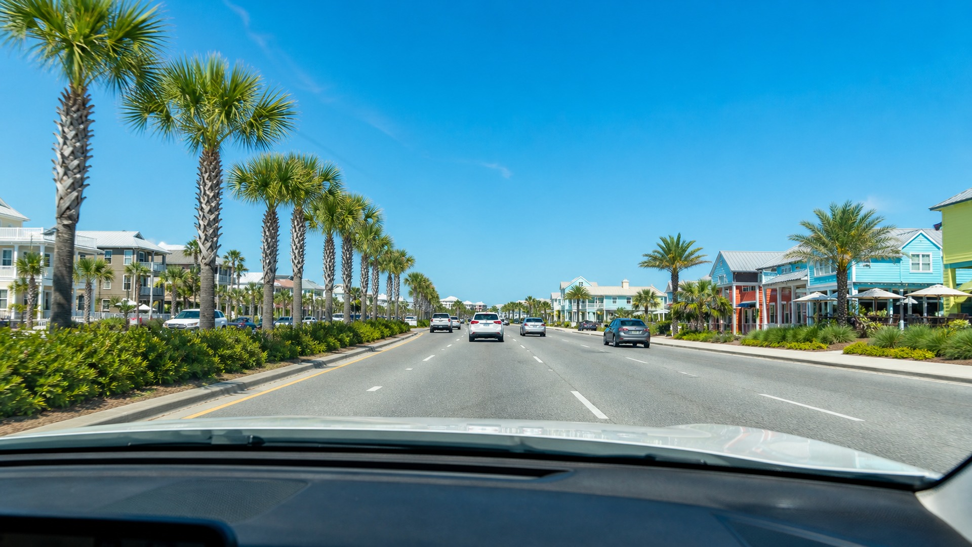 View from inside a car driving west on US-98 Emerald Coast Parkway entering Destin Florida in summer with beach shops and bright blue sky